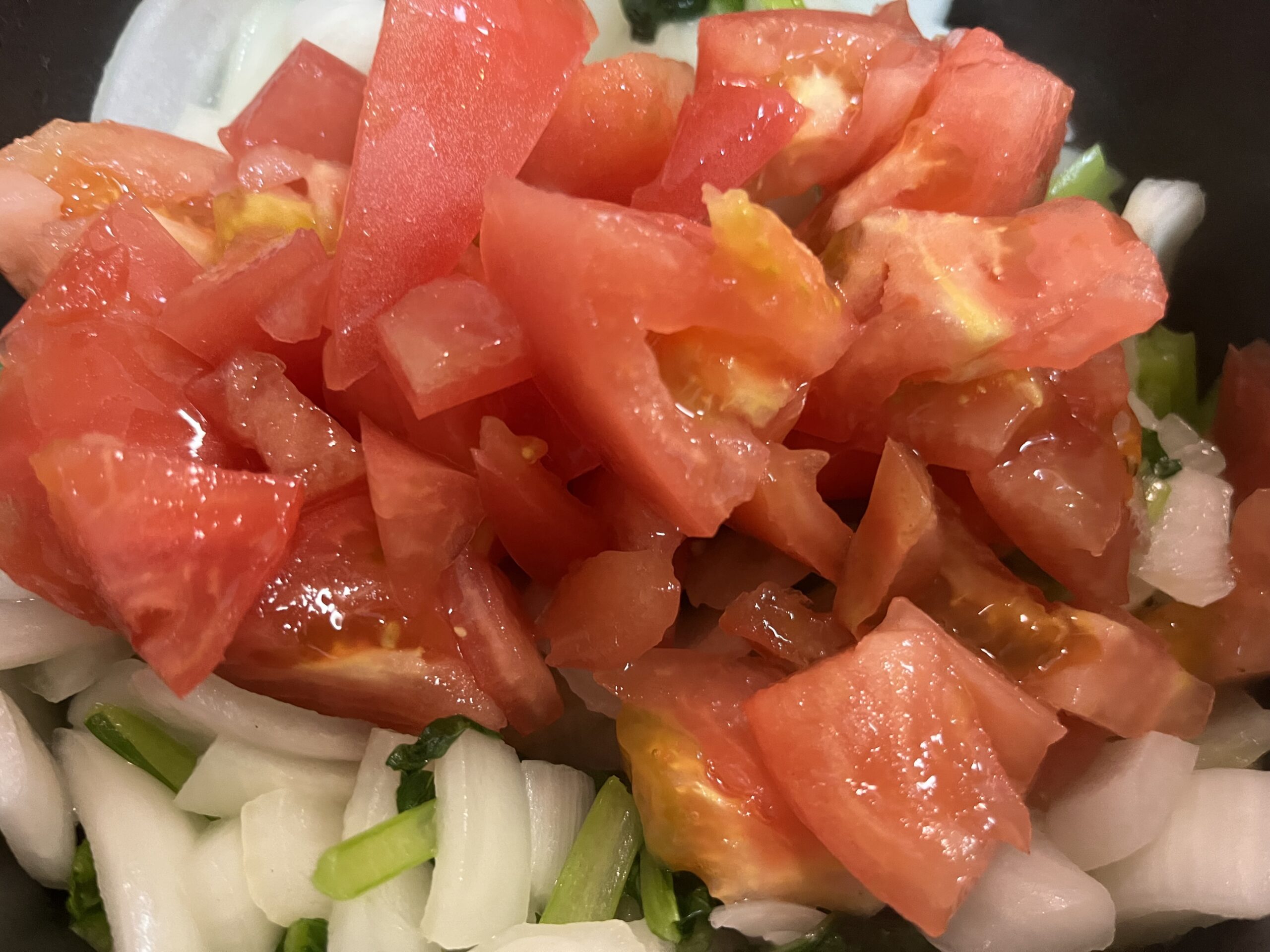玉ねぎ、小松菜、トマトを細かく切り炒める様子を撮影した写真